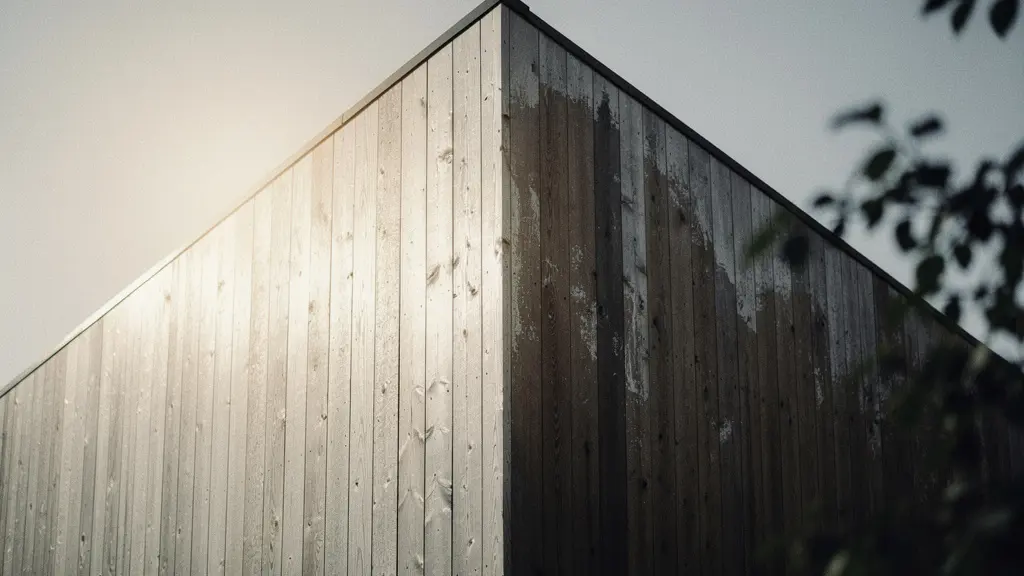Angle d une maison en bardage bois montrant une face ensoleillee grisonnante et une face ombragee avec des zones plus sombres liees a l humidite